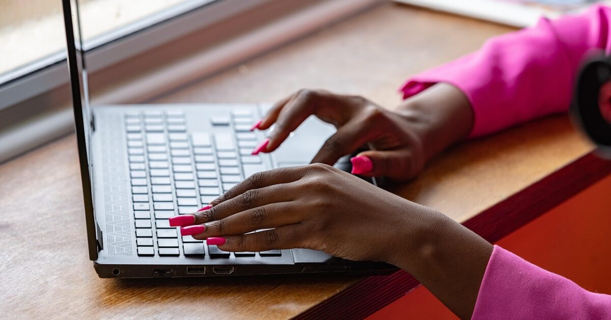 ピンクのネイルをした女性がノートパソコンを操作しているクローズアップ