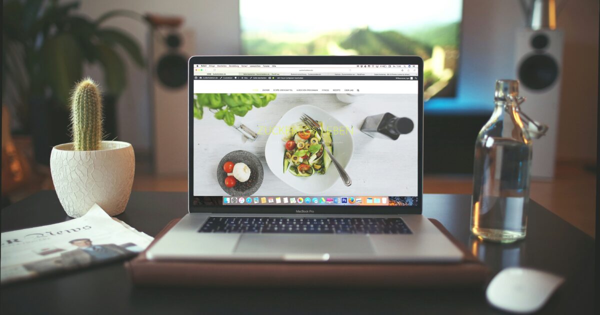ノートパソコンに料理の写真付きウェブサイトが表示されているホームオフィスの様子